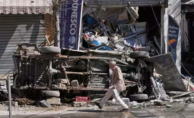 A man passes by a destroyed car and shop on a commercial street that was hit by Israeli airstrikes in Nabatiyeh town, south Lebanon, Thursday, March 5, 2026. (AP Photo/Mohammed Zaatari)
