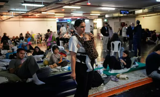 Leah Guttmann holds her son, Teddy, as other people take shelter in an underground parking garage while air-raid sirens warn of incoming missiles launched by Iran toward Tel Aviv, Israel, Sunday, March 1, 2026. (AP Photo/Ohad Zwigenberg)
