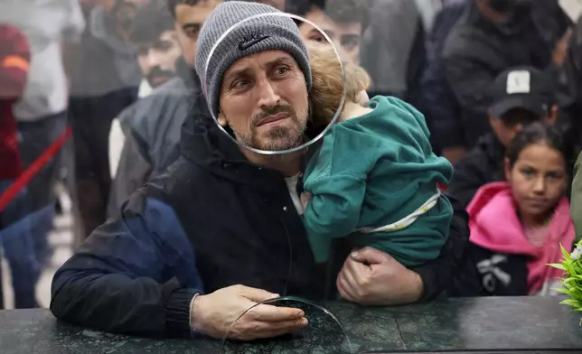 A Syrian man carries a child as they cross the Syrian-Lebanese border into Syria, fleeing Lebanon due to Israeli airstrikes, in Jdeidet Yabous, Syria, Tuesday, March 3, 2026. (AP Photo/Ghaith Alsayed)
