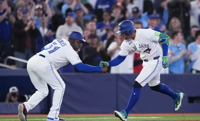 Toronto Blue Jays designated hitter George Springer (4) celebrates his solo home run with Toronto Blue Jays third base coach Carlos Febles (51) while playing against the Athletics during first inning American League baseball action in Toronto on Sunday, March 29, 2026. (Nathan Denette/The Canadian Press via AP)