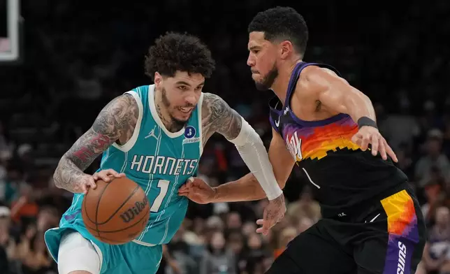 Charlotte Hornets guard LaMelo Ball (1) drives on Phoenix Suns guard Devin Booker during the second half of an NBA basketball game, Sunday, March 8, 2026, in Phoenix. (AP Photo/Rick Scuteri)