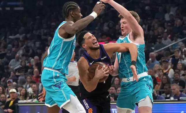 Phoenix Suns guard Devin Booker drives between Charlotte Hornets forward Moussa Diabate and guard Kon Knueppel (7) during the first half of an NBA basketball game, Sunday, March 8, 2026, in Phoenix. (AP Photo/Rick Scuteri)