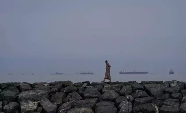 FILE - A man walks along the shore as oil tankers and cargo ships line up in the Strait of Hormuz, as seen from Khor Fakkan, United Arab Emirates, Wednesday, March 11, 2026. (AP Photo/Altaf Qadri, file)