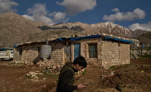 Bilal Osman, 25, an Iraq-Iran cross-border smuggler, speaks on the phone with a partner in Iran as he stands at a compound in a village in the mountainous Kurdish region near Halabja, Iraq, Tuesday, March 17, 2026. (AP Photo/Leo Correa)