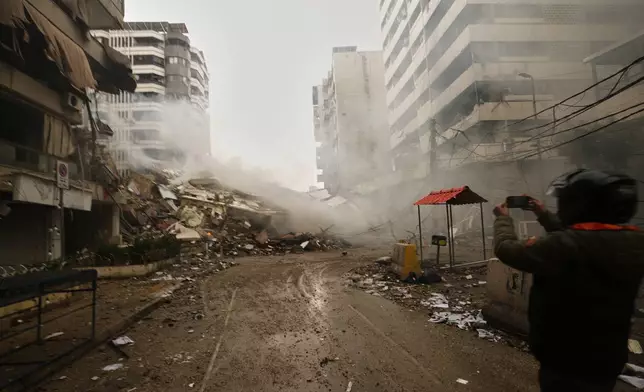 A man photographs the rubble of buildings destroyed in an Israeli airstrike in Dahiyeh, Beirut's southern suburbs, Lebanon, Sunday, March 15, 2026. (AP Photo/Hassan Ammar)