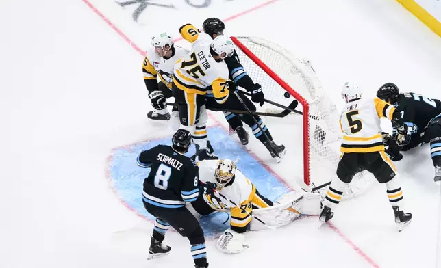 The puck deflects off of Utah Mammoth right wing Dylan Guenther, center top, and into the net during the first period of an NHL hockey game against the Pittsburgh Penguins, Saturday, March 14, 2026, in Salt Lake City. (AP Photo/Tyler Tate)