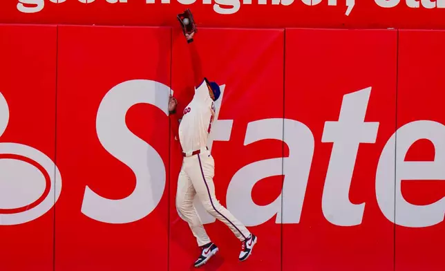 Philadelphia Phillies center fielder Justin Crawford leaps to catch the fly ball by Texas Rangers' Wyatt Langford during the third inning of a baseball game, Saturday, March 28, 2026, in Philadelphia. (AP Photo/Chris Szagola)
