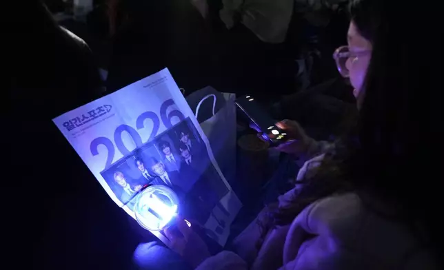 A fan of K-pop band BTS reads a newspaper reporting the comeback of BTS before a drone light show to celebrate, at a park along the Han River in Seoul, South Korea, Friday, March 20, 2026. (AP Photo/Lee Jin-man)