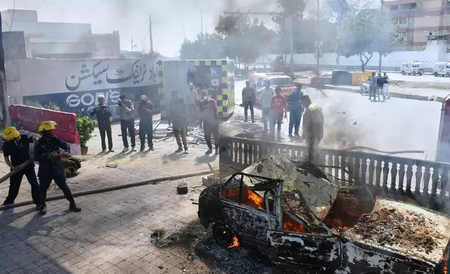 Firefighters pour water on a burning car, which was set on fire by protestors close to the U.S. Consulate in Karachi, Pakistan, Sunday, March 1, 2026. (AP Photo/Ali Raza)
