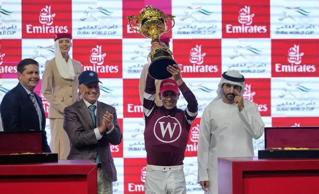 Jockey Jose Ortiz, second right, holds the trophy after riding Magnitude to win the $12 million Dubai World Cup over 2000m (10 furlongs) at Meydan Racecourse in Dubai, the United Arab Emirates, Saturday, March 28, 2026. At left is owner Ron Winchell, and assistant trainer Scott Blasi. (AP Photo/Altaf Qadri)