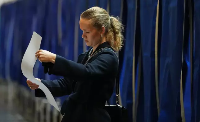 A woman holds a ballot at a polling station at City Hall in Copenhagen, Denmark, on Tuesday, March 24, 2026, during the general election. (AP Photo/Sergei Grits)