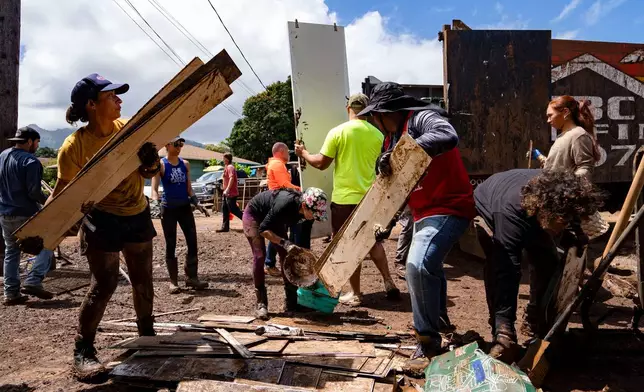 Volunteers load debris and damaged household items onto a truck during cleanup efforts following flooding, Tuesday, March 24, 2026, in Waialua, Hawaii. (AP Photo/Mengshin Lin)