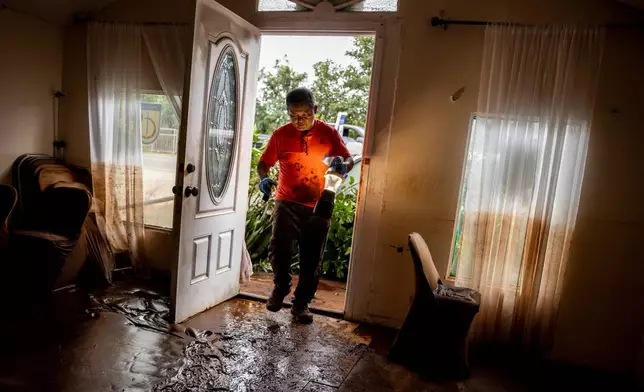 Glenn Duquez, associate pastor at the Church of God Jesus is Alive Fellowship, carries a lamp into the mud-riddled church building to clean up after the fast-moving flood in Haleiwa, Hawaii Saturday, March 21, 2026. (Stephen Lam/San Francisco Chronicle via AP)