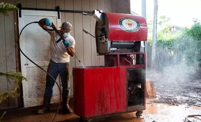 Nate Knaggs pressure washes a coffee roaster at his home damaged by flooding, Tuesday, March 24, 2026, in Haleiwa, Hawaii. (AP Photo/Mengshin Lin)