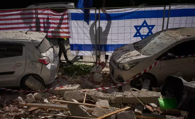 Israeli authorities hang Israeli and U.S. flags at the site struck by an Iranian missile that killed two people, in Ramat Gan, Israel, Wednesday, March 18, 2026. (AP Photo/Oded Balilty)