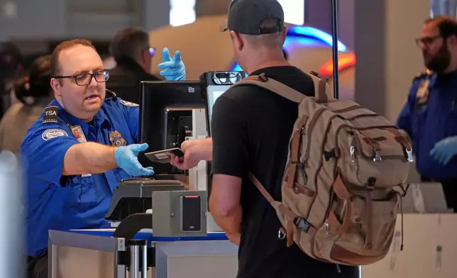 A TSA worker hands a passport back to a traveler at a TSA checkpoint in Pittsburgh International Airport in Imperial, Pa., Monday, March 23, 2026. (AP Photo/Gene J. Puskar)