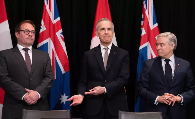 Canada's Prime Minister Mark Carney, center, gestures to Daniel Mulino, Australian Assistant Treasurer as he is introduced at the start of a signing ceremony, as Canada's Finance and National Revenue Minister Francois-Philippe Champagne, right, looks on, in Sydney, Australia, Wednesday, March 4, 2026. (Adrian Wyld/The Canadian Press via AP)
