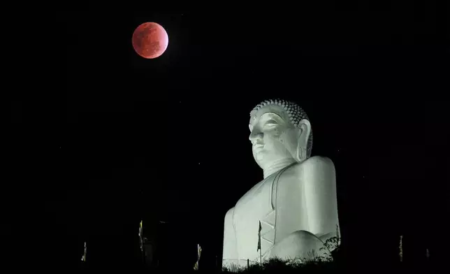 FILE - A lunar eclipse in the night sky behind a statue of the Buddha in Kurunegala, Sri Lanka, Saturday, Dec. 10, 2011. (AP Photo/ Eranga Jayawardena, File)