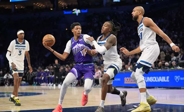 Utah Jazz guard Ace Bailey (19), second left, works toward the basket as Minnesota Timberwolves guard Ayo Dosunmu (13), second right, and center Rudy Gobert (27), right, defend during the first half of an NBA basketball game, Wednesday, March 18, 2026, in Minneapolis. (AP Photo/Abbie Parr)