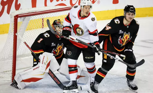 Ottawa Senators' Nick Cousins, centre, is checked by Calgary Flames' Brayden Pachal, right, in front of goalie Devin Cooley during the second period of an NHL hockey game in Calgary on Thursday, March 5, 2026. (Jeff McIntosh/The Canadian Press via AP)