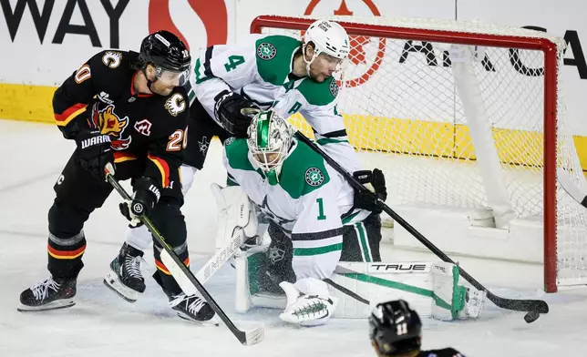 Dallas Stars' Miro Heiskanen (4) reaches over goalie Casey DeSmith (1) to swat the puck away as Calgary Flames' Blake Coleman looks on during the second period of an NHL hockey game in Calgary, Alberta on Tuesday, March 3, 2026. (Jeff McIntosh/The Canadian Press via AP)
