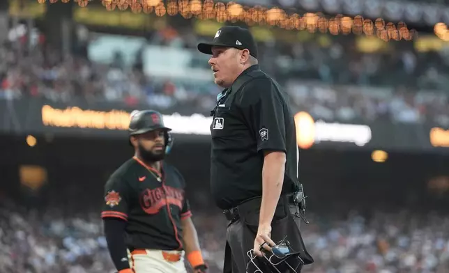 Umpire Chad Whitson, right, announces that San Francisco Giants' Heliot Ramos, left, challenged a strike, which was overturned, during the ninth inning of a baseball game between the Giants and the New York Yankees in San Francisco, Saturday, March 28, 2026. (AP Photo/Jeff Chiu)