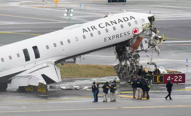 Officials with the National Transportation Safety Board investigate the site, Monday, March 23, 2026, where an Air Canada jet came to rest after colliding with a Port Authority firetruck at LaGuardia Airport, shortly after landing Sunday night in New York. (AP Photo/Seth Wenig)