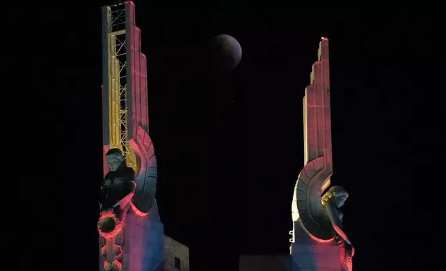 A total lunar eclipse is seen through statues at the Quezon Memorial Shrine in Quezon City, Philippines, Tuesday, March 3, 2026. (AP Photo/Aaron Favila)