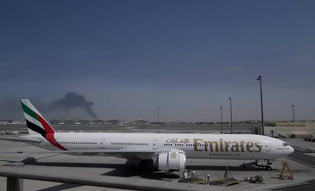 ADDS CAUSE OF BLACK SMOKE IN THE BACKGROUND.- A plume of smoke caused by an Iranian strike is seen in the background an an Emirates plane is parked at the Dubai International Airport after its closure in Dubai, United Arab Emirates, Sunday, March 1, 2026. (AP Photo/Altaf Qadri)