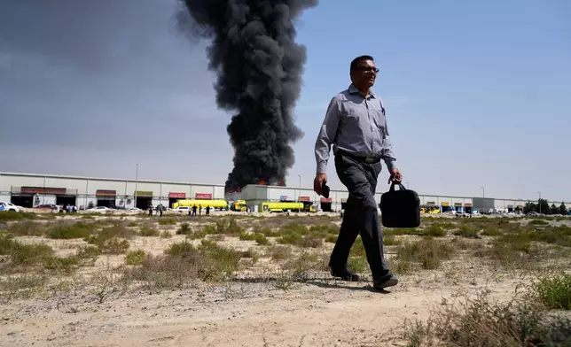 A man walks away after watching as a black plume of smoke rises from a warehouse in the industrial area of Sharjah City, United Arab Emirates, Sunday, March 1, 2026, following reports of Iranian strikes in Dubai. (AP Photo/Altaf Qadri)