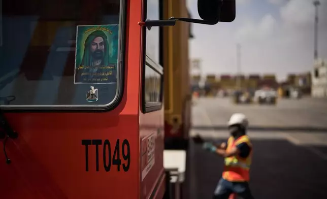 An image depicting Ali ibn Abi Talib, the cousin and son-in-law of the Prophet Muhammad, who is revered by Muslims particularly Shiite sect, is displayed on the windshield of a truck as dockworkers unload cargo containers at Umm Qasr Port, a deep-water port, in the city of Umm Qasr, Iraq, Friday, March 27, 2026. (AP Photo/Leo Correa)