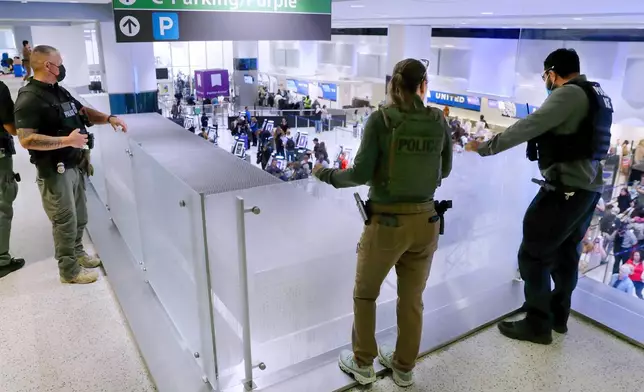 Federal immigration agents peer over railings on the floor above the lines of air travelers progressing to the TSA security checkpoint in Terminal C at the George Bush Intercontinental Airport, Monday, March 23, 2026, in Houston. (AP Photo/Michael Wyke)
