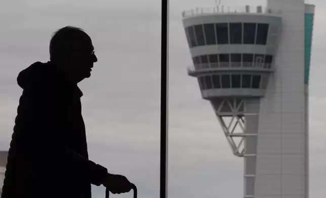 A traveler moves in view of an air traffic control tower at Philadelphia International Airport in Philadelphia, Friday, March 27, 2026. (AP Photo/Matt Rourke)