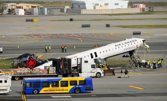 Officials inspect the wreckage of an Air Canada Express jet, Wednesday, March 25, 2026, just off the runway where it had collided with a Port Authority fire truck Sunday night at LaGuardia Airport in New York. (AP Photo/Yuki Iwamura)
