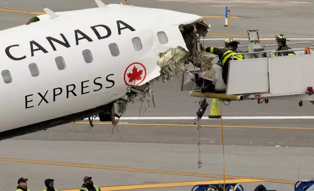 Airport firefighters remove loose debris from the wreckage of an Air Canada Express jet, Wednesday, March 25, 2026, just off the runway where it had collided with a Port Authority fire truck Sunday night at LaGuardia Airport in New York. (AP Photo/Yuki Iwamura)