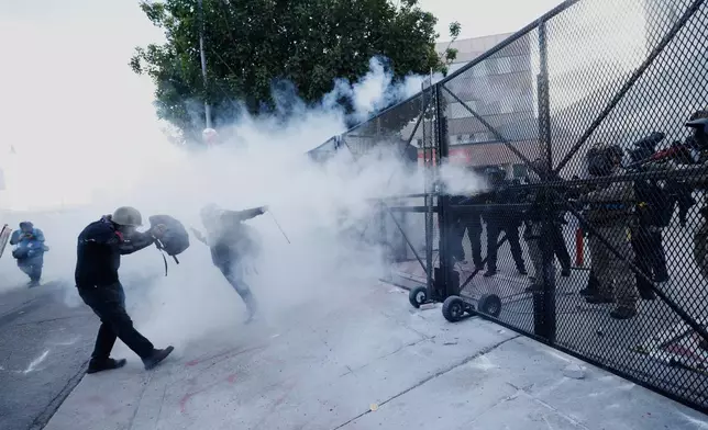 Demonstrators take cover as police fire tear gas outside the Metropolitan Detention Center in downtown Los Angeles during a "No Kings" protest Saturday, March 28, 2026. (AP Photo/Jill Connelly)