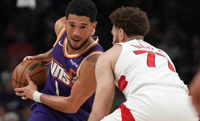 Phoenix Suns guard Devin Booker shields the ball from Toronto Raptors forward Jamison Battle (77) during the first half of an NBA basketball game, Sunday, March 23, 2026, in Phoenix. (AP Photo/Rick Scuteri)