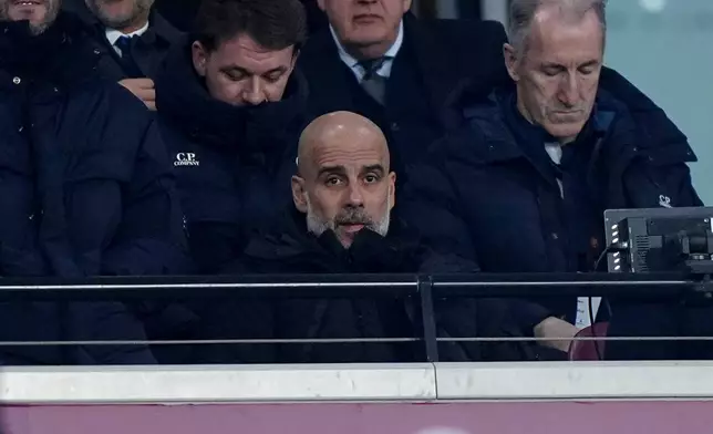 Manchester City manager Pep Guardiola, center, watches from the stands during the Premier League soccer match against West Ham United, Saturday, March 14, 2026, in London. (Bradley Collyer/PA via AP)