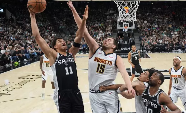 San Antonio Spurs forward Carter Bryant (11) drives to the basket against Denver Nuggets center Nikola Jokic (15) during the first half of an NBA basketball game in San Antonio, Thursday, March 12, 2026. (AP Photo/Eric Gay)