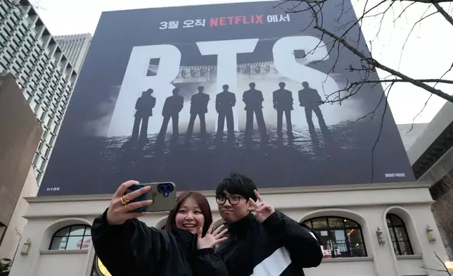 A couple takes a selfie photo near a banner promoting a comeback concert of K-pop group BTS at Gwanghwamun Square in Seoul, Wednesday, March 18, 2026. (AP Photo/Ahn Young-joon)