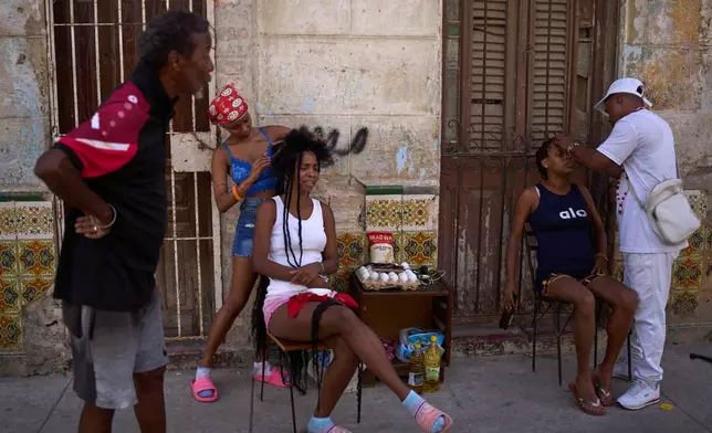 Hairdressers style the hair of their clients in the open air during a blackout in Havana, Cuba, Thursday, March 5, 2026. (AP Photo/Ramon Espinosa)