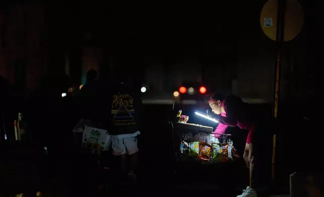 A vendor lights her way with a battery-powered lamp while waiting for customers on the Malecón during a blackout in Havana, Cuba, Saturday, March 21, 2026. (AP Photo/Ramon Espinosa)