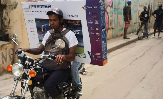 A motorcyclist transports a customer with a television in a box during a blackout in Havana, Tuesday, March 17, 2026. (AP Photo/Ramon Espinosa)