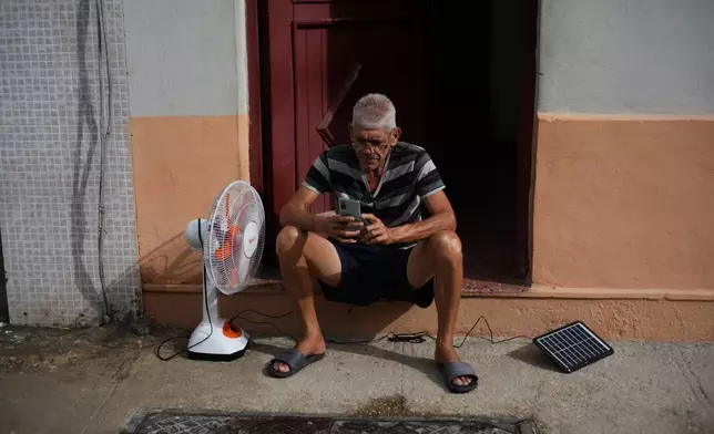 A man charges his phone and his fan with a solar panel during a blackout in Havana, Tuesday, March 17, 2026. (AP Photo/Ramon Espinosa)