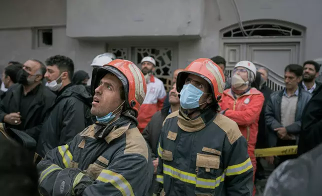 Firefighters look on as volunteers and first responders inspect the rubble and search for victims at a residential building hit in an overnight strike during the U.S.-Israeli military campaign in Tabriz, East Azerbaijan Province, northwestern Iran, Tuesday, March 24, 2026. (AP Photo/Matin Hashemi)