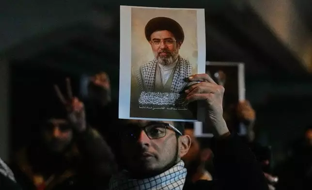 Iraqis hold a portrait of the new successor to Supreme Leader, Ayatollah Mojtaba Khamenei at a bridge leading to the fortified Green Zone where the U.S. embassy is located in Baghdad, Iraq, Monday, March 9, 2026. (AP Photo/Hadi Mizban)
