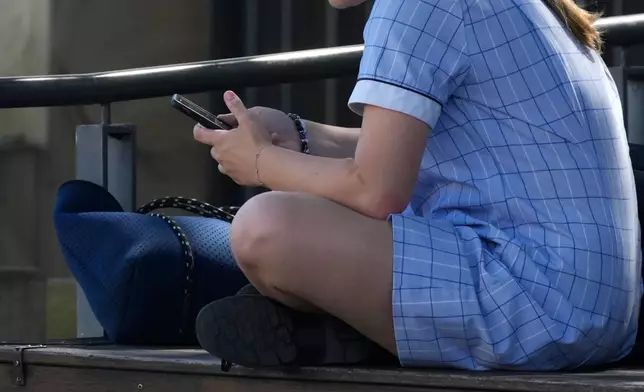 FILE - A young girl uses her phone while sitting on a bench in Sydney, Nov. 8, 2024. (AP Photo/Rick Rycroft, File)