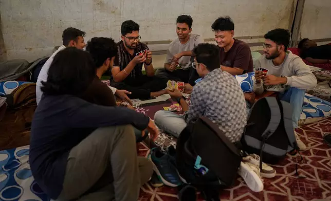 Stranded Indian travelers play cards as they sit inside a tent at a farmhouse owned by an Indian businessman, now converted into a shelter in Ajman, near Dubai, United Arab Emirates, Saturday, March 7, 2026. (AP Photo/Altaf Qadri)