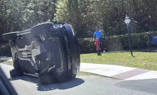 Golfer Tiger Woods stands by his overturned vehicle in Jupiter Island, Fla., on Friday, March 27, 2026. (AP Photo/Jason Oteri)