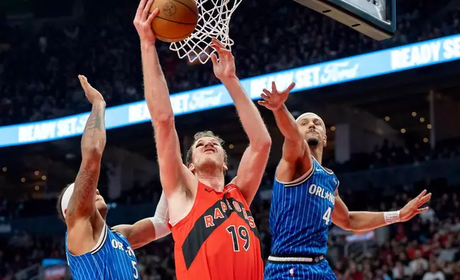 Toronto Raptors centre Jakob Poeltl (19) drives to the hoop past Orlando Magic guard Jalen Suggs (4) and forward Paolo Banchero (5) during first half NBA action in Toronto on Sunday, March 29, 2026. (Frank Gunn/The Canadian Press via AP)